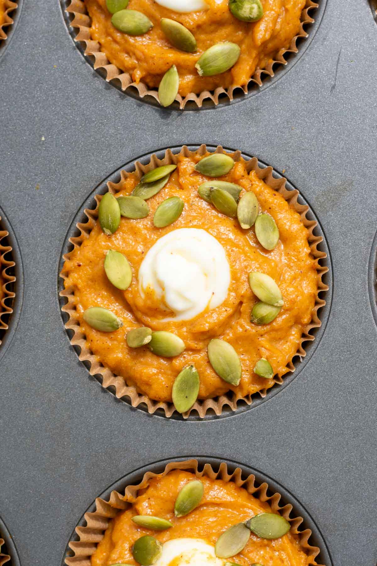 A sourdough pumpkin cream cheese muffin with pumpkin seeds in a muffin pan before baking.