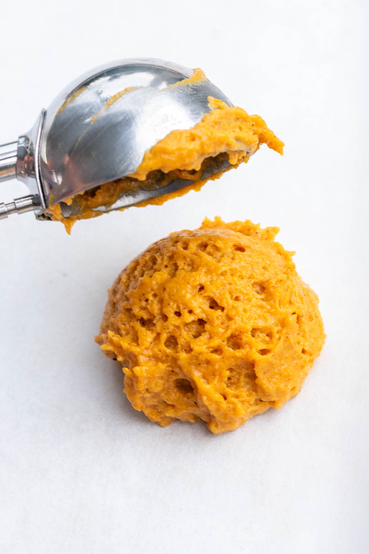 Scoop of sourdough pumpkin whoopie pie batter on parchment paper with a cookie scoop