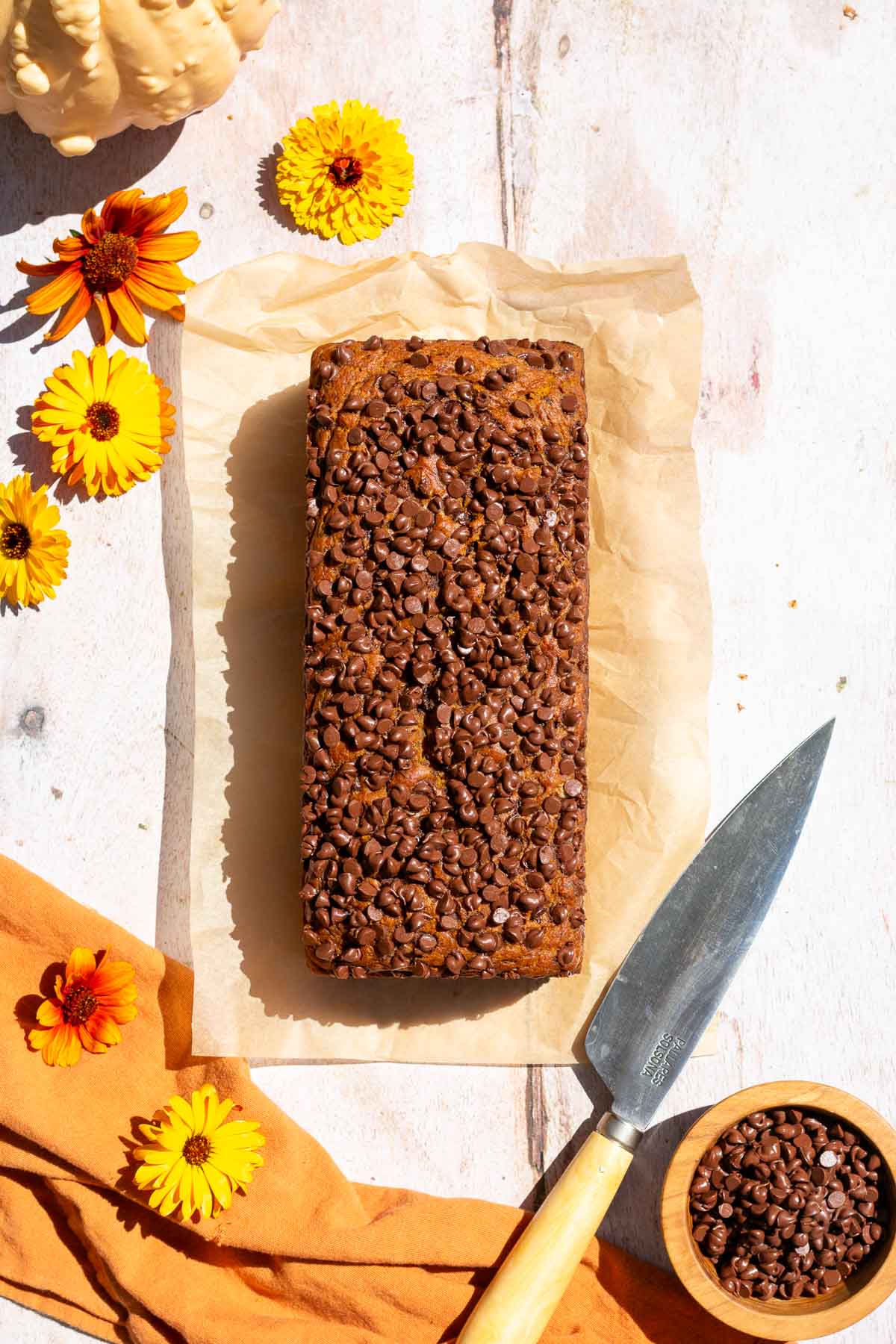 Baked sourdough pumpkin chocolate chip bread on parchment paper cooling with a knife.