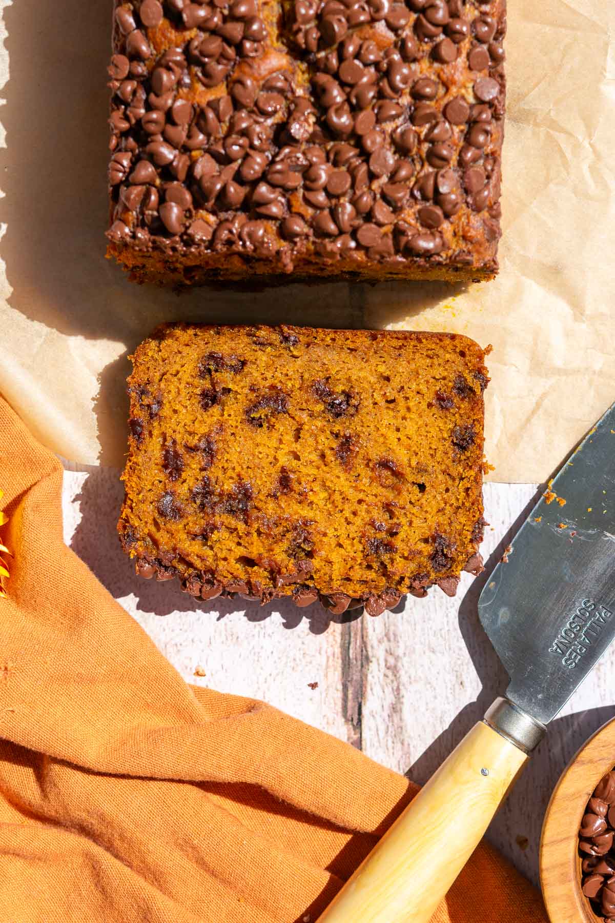 Cut slice of sourdough pumpkin chocolate chip bread with an orange towel and knife.