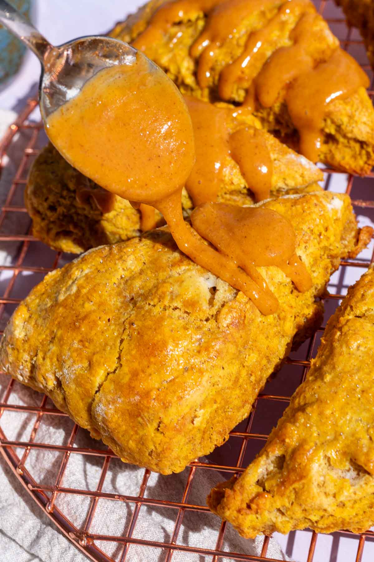 Drizzling the pumpkin glaze on top of baked sourdough pumpkin scones on a wire rack with a spoon.