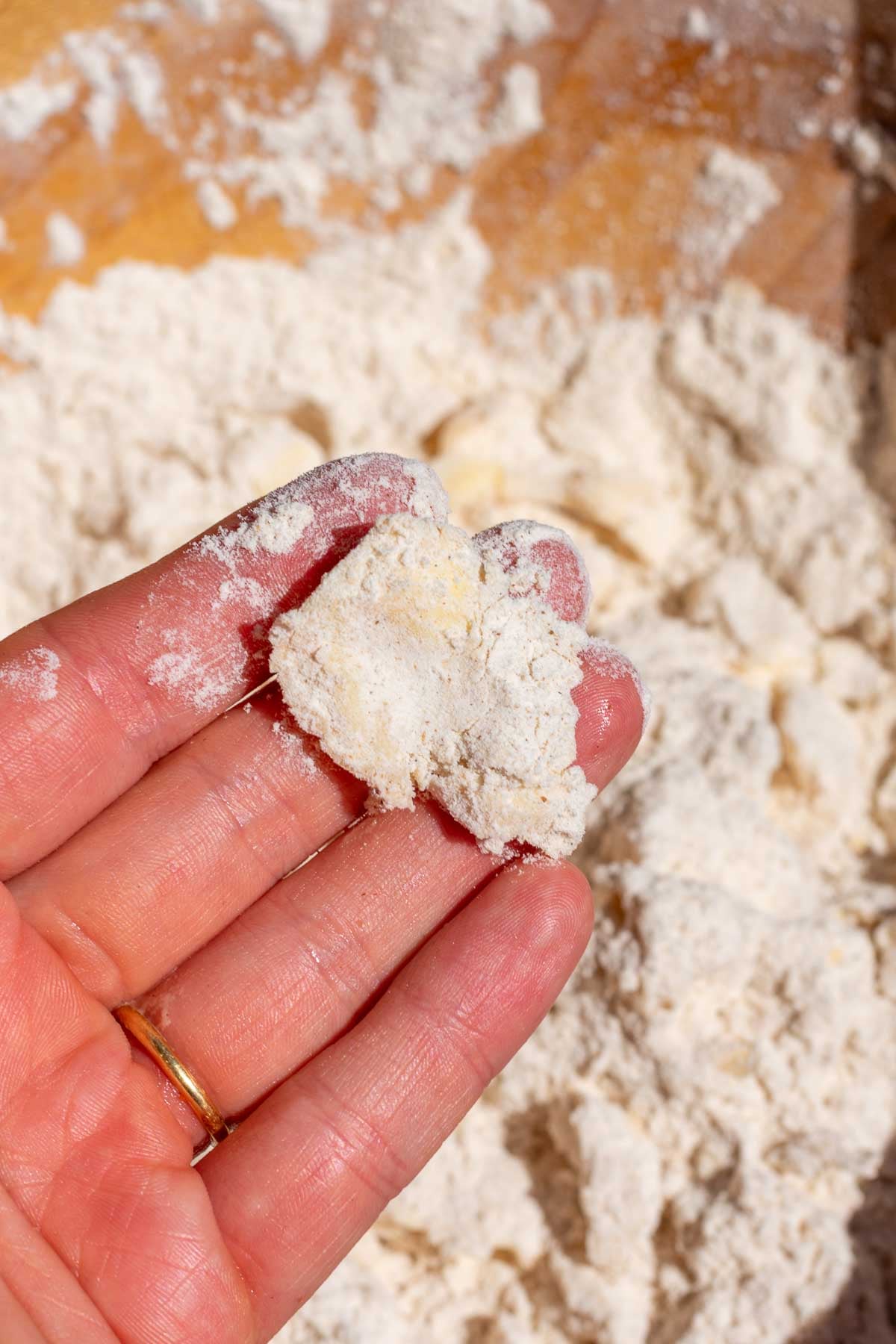 Hand holding a smashed piece of butter with the dry ingredients for scones.