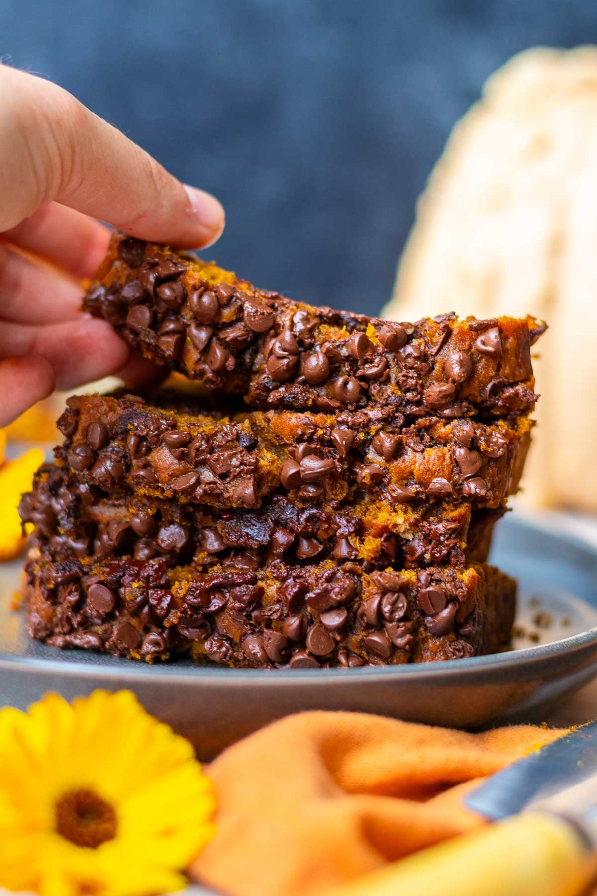 Hand picking up a slice of a stack of sourdough pumpkin chocolate chip bread slices on a plate.