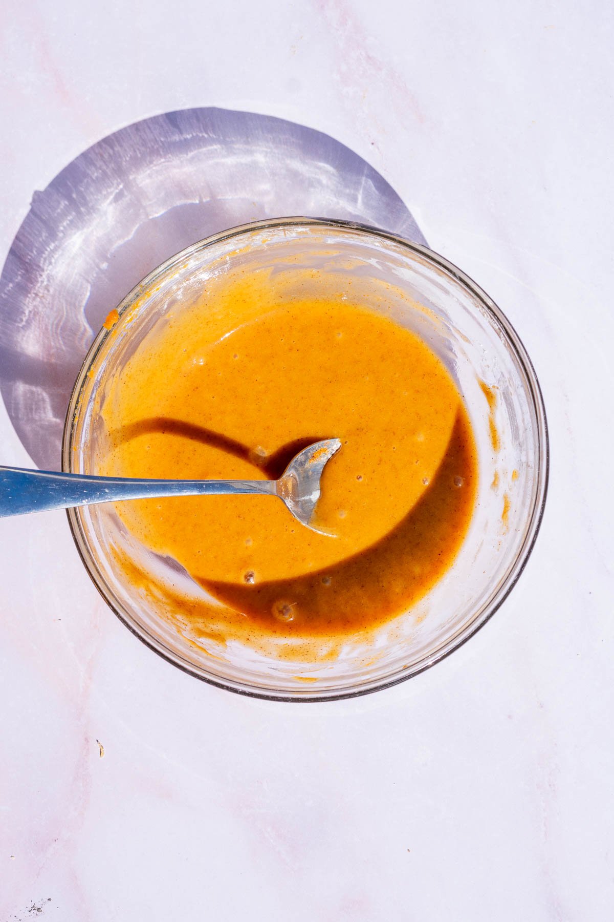 Bowl of pumpkin cinnamon glaze with a spoon.