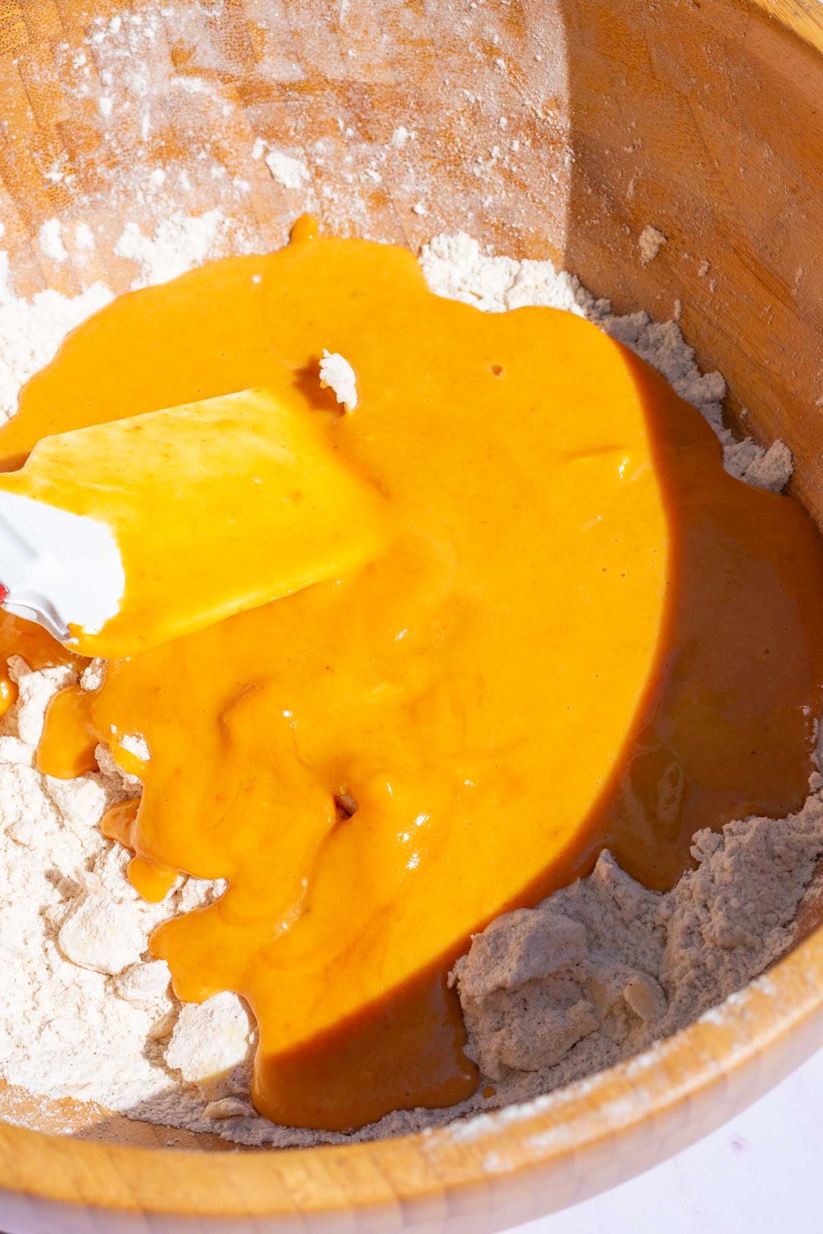 Wooden bowl with wet ingredients poured on top of dry ingredients for pumpkin scones with a spatula in the bowl.