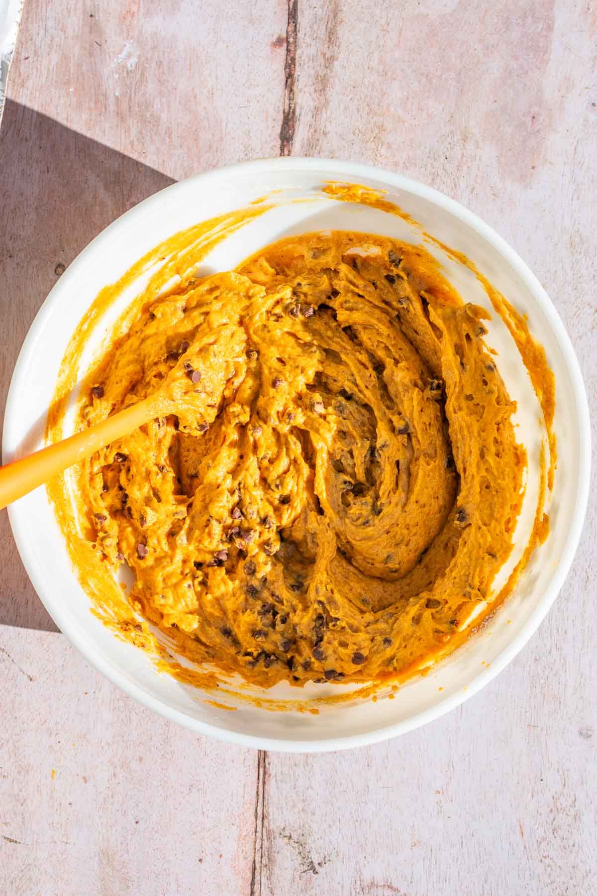 Folding in chocolate chips to sourdough pumpkin bread batter in a bowl with a spatula.