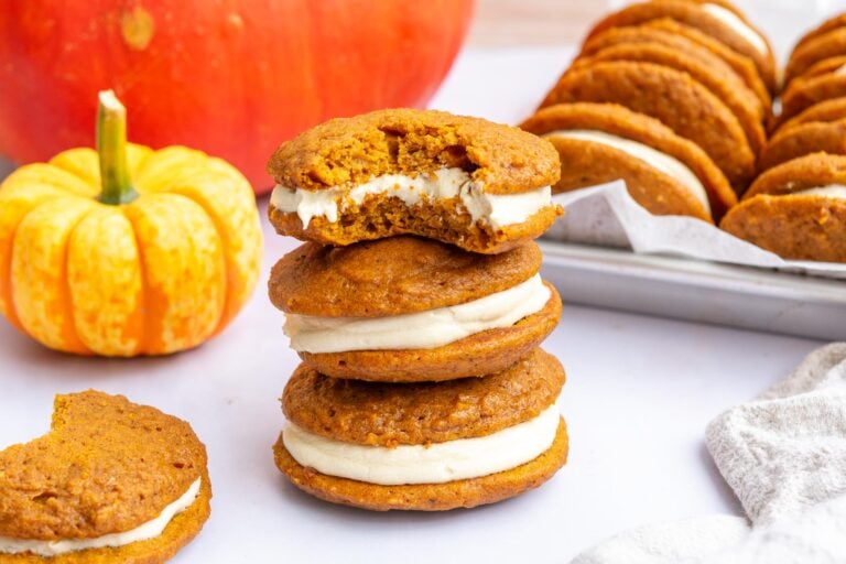 Sourdough pumpkin whoopie pies with salted maple buttercream stacked on top of each other with pumpkins in the background.