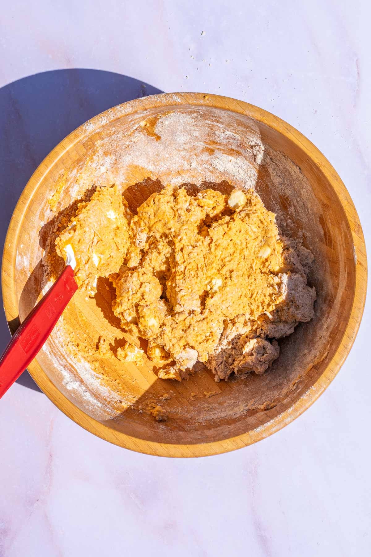 Mixed sourdough pumpkin scones dough in wooden bowl with a spatula.