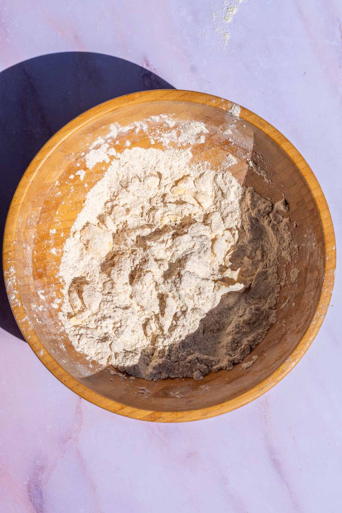 Large wooden bowl of dry ingredients and butter mixed together for sourdough pumpkin scones.