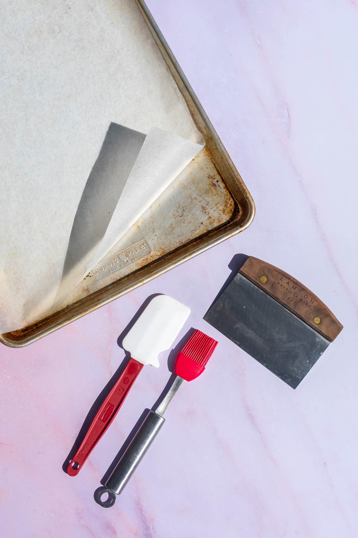 Tools needed for sourdough pumpkin scones including a bench scraper, sheet pan with parchment paper, spatula, and a pastry brush.
