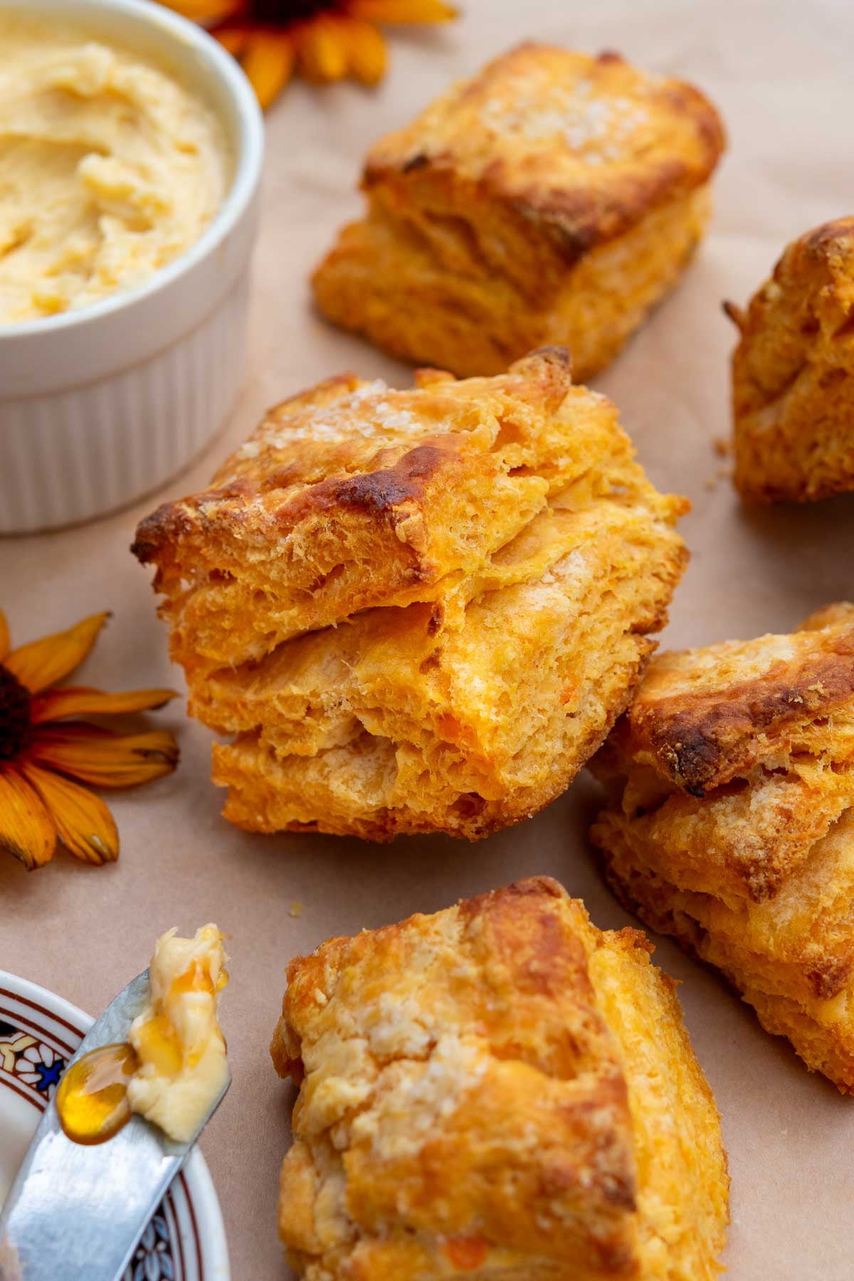 Close up of a flaky sourdough sweet potato biscuit on parchment paper with hot honey butter.