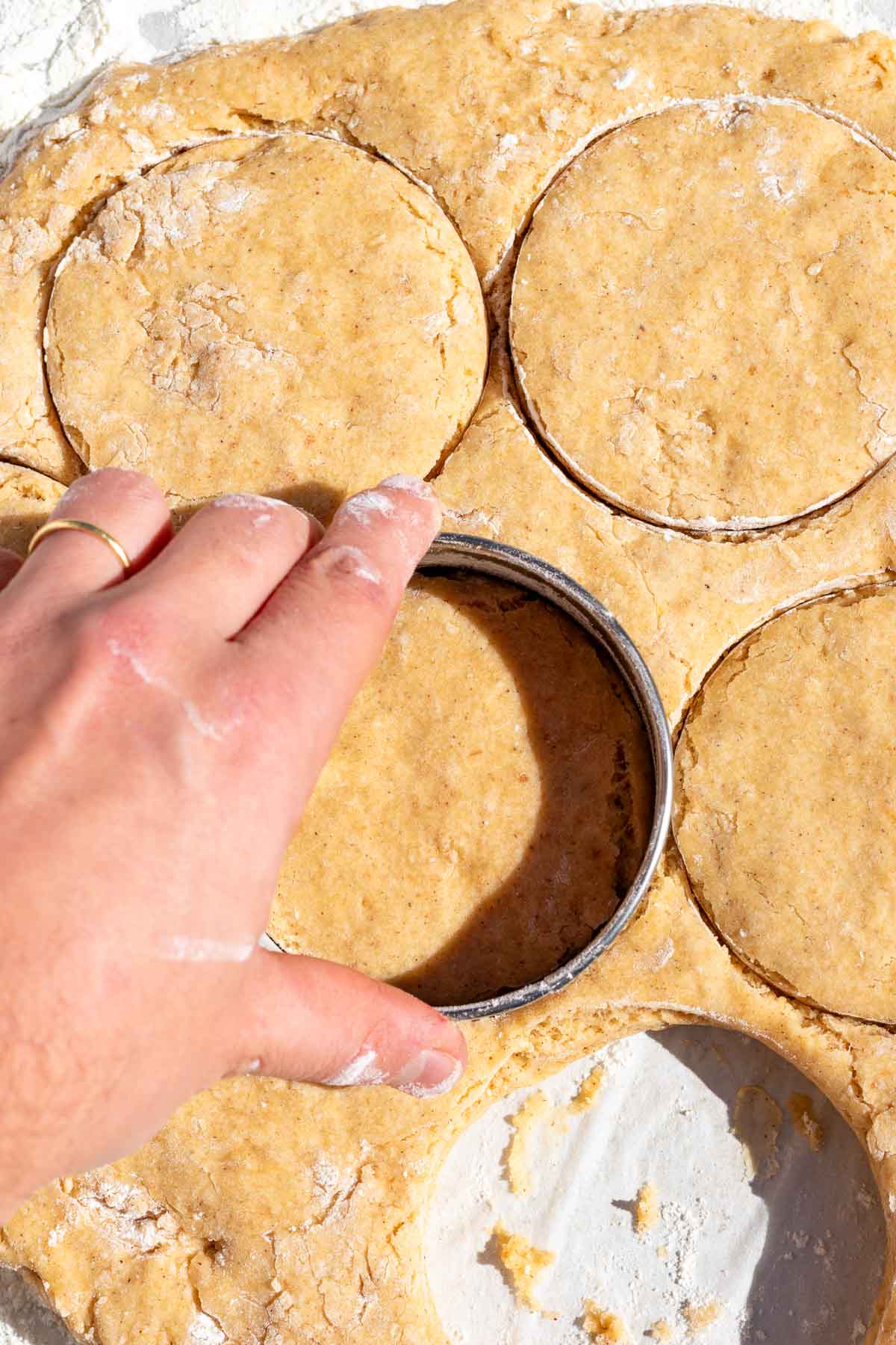 Hand using a cookie cutter to cut out rounds from donut batter.