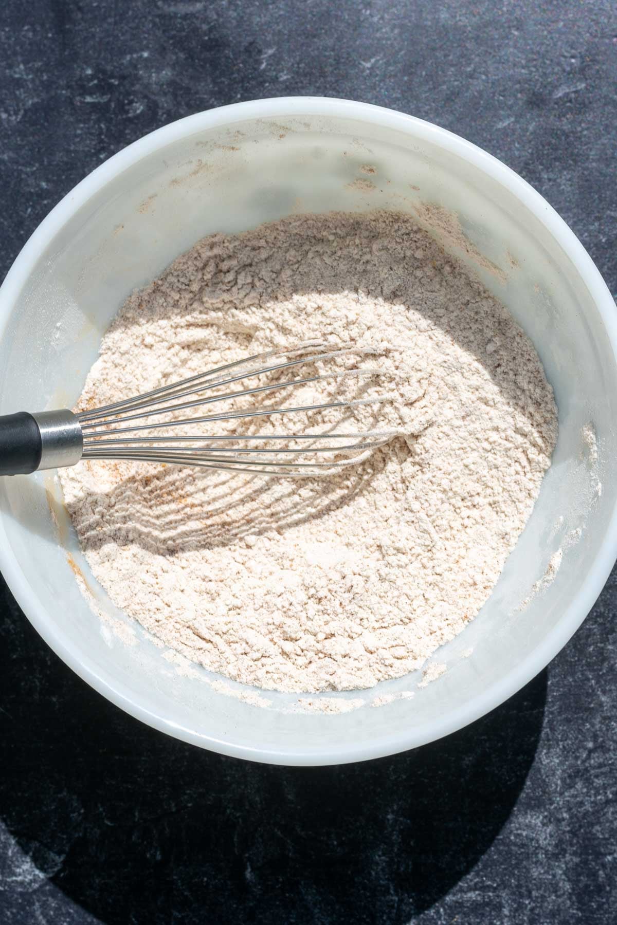 Bowl with mixed dry ingredients for sourdough apple cider donuts with a whisk.