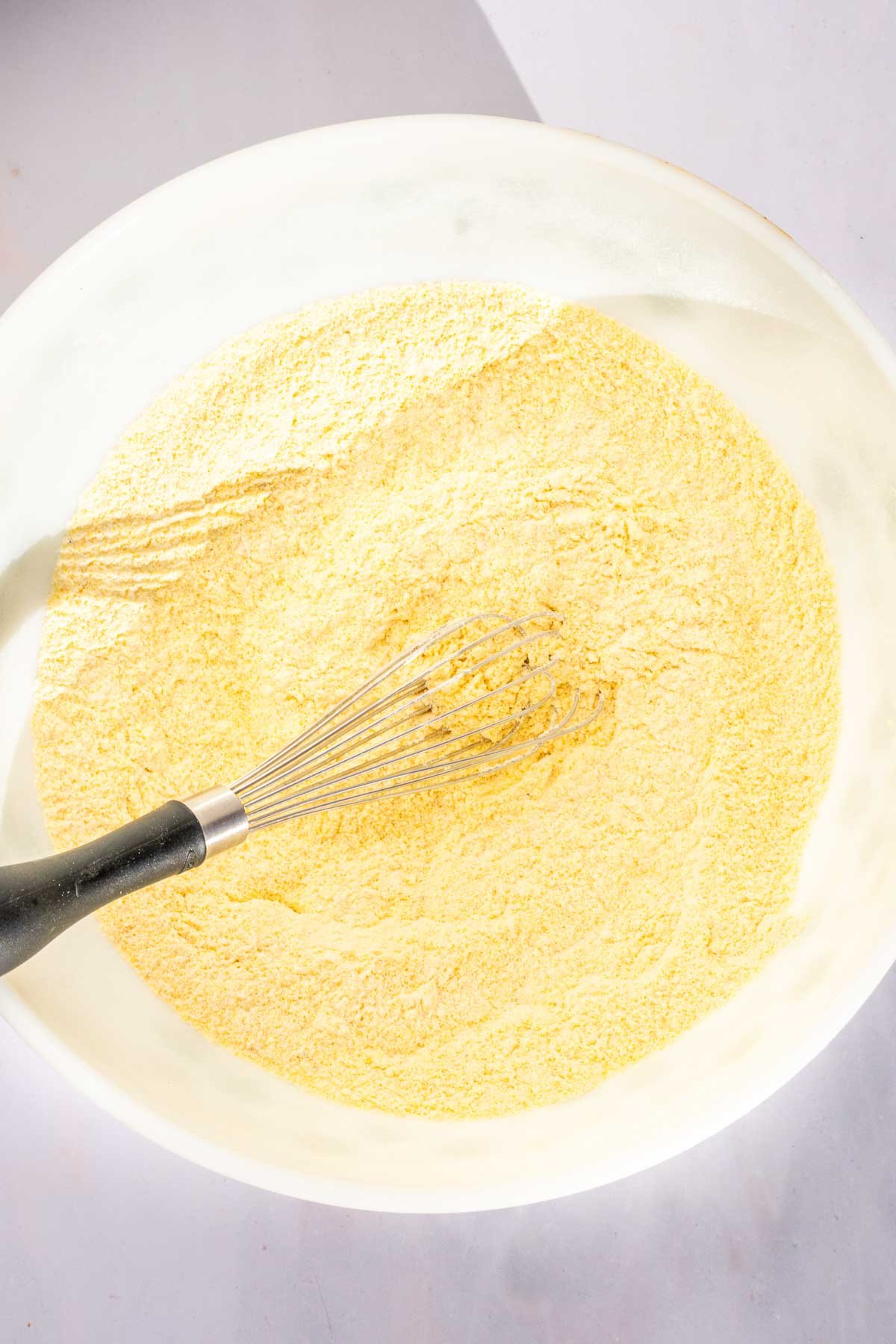 Bowl of mixed dry ingredients for sourdough corn muffins with a whisk.