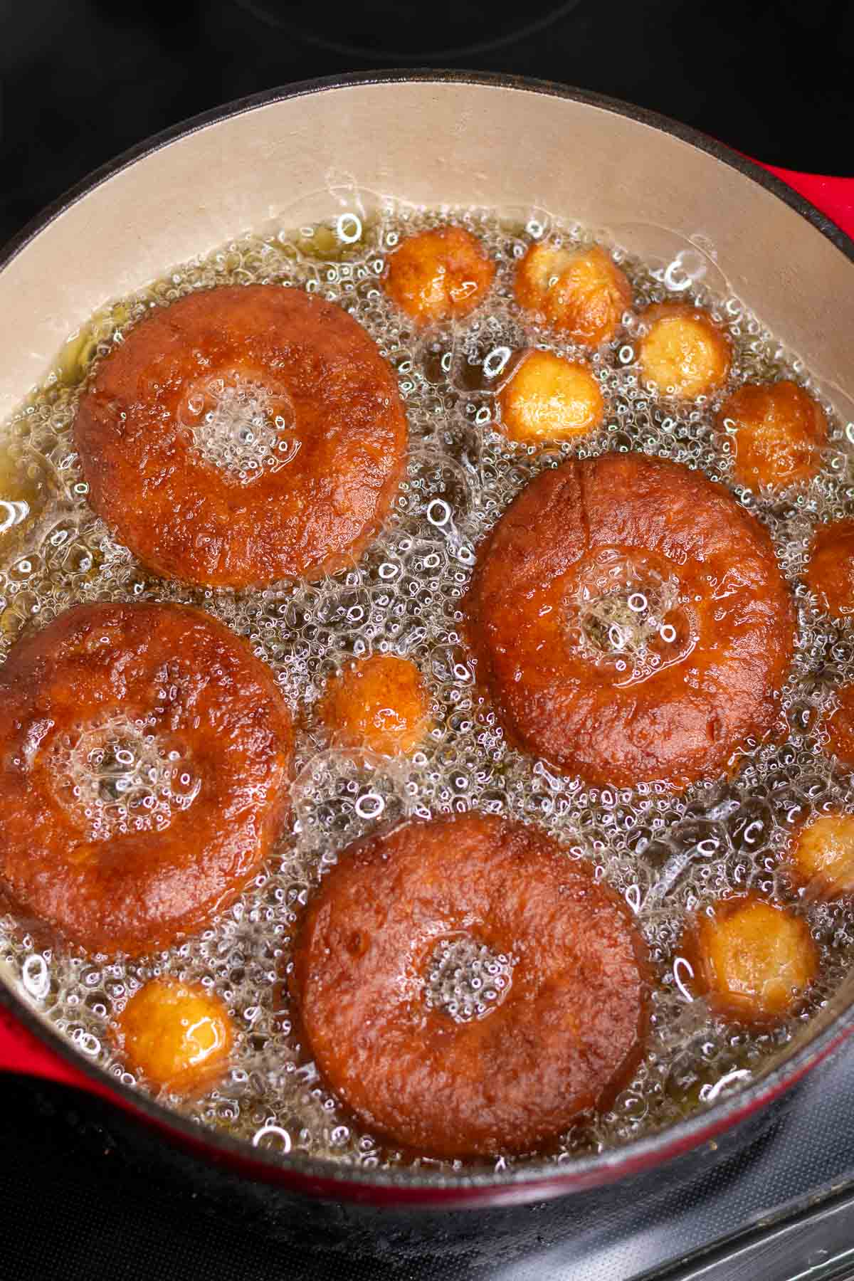 Flipped and browned sourdough apple cider donuts in a pot of hot frying oil.