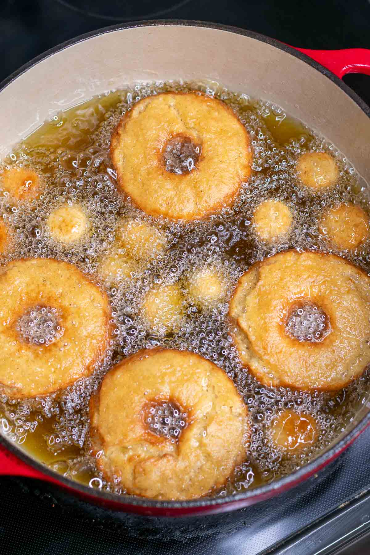Sourdough apple cider donuts and donut holes in a pot of frying oil.