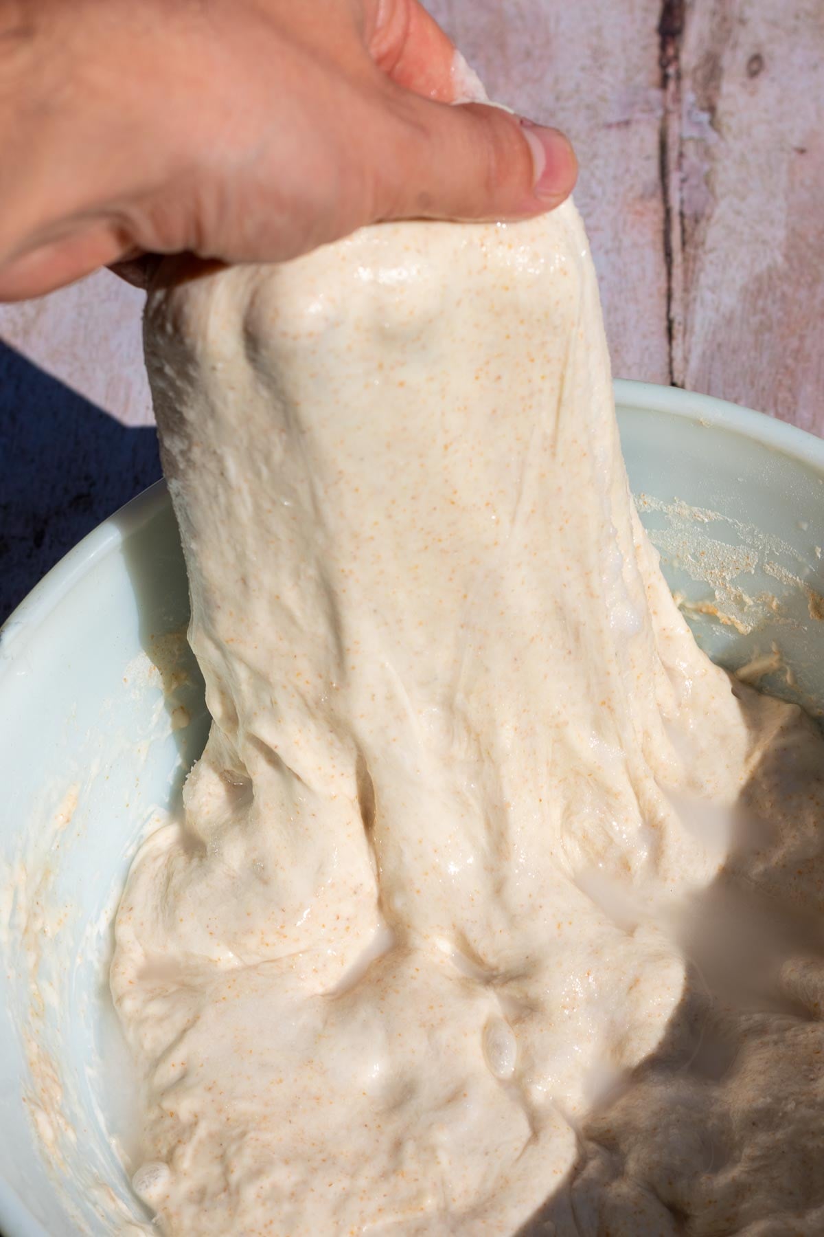 Hand lifting and stretching dough in mixing bowl.