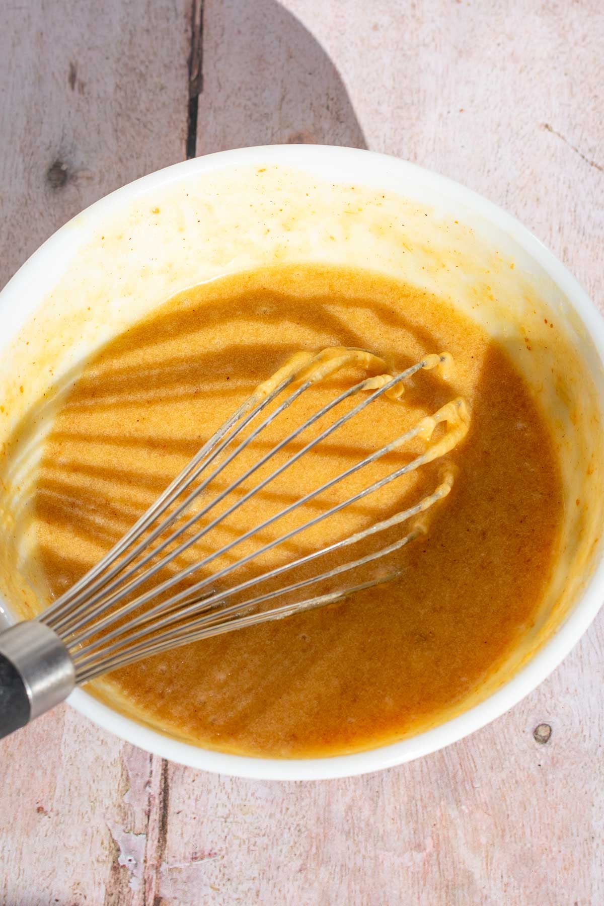 Mixed wet ingredients for sourdough apple cider donuts in a bowl with a  whisk.