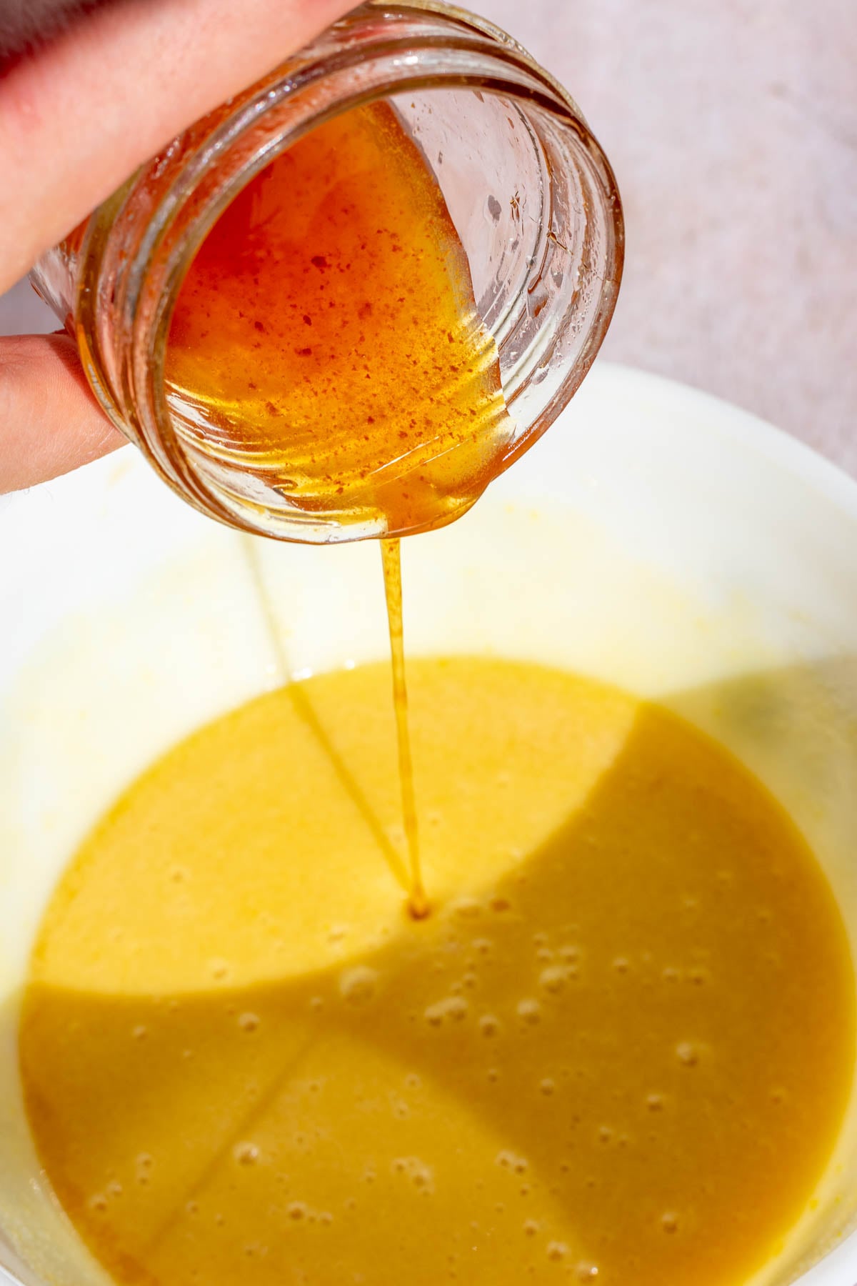 Pouring boiled apple cider into a bowl with wet ingredients.