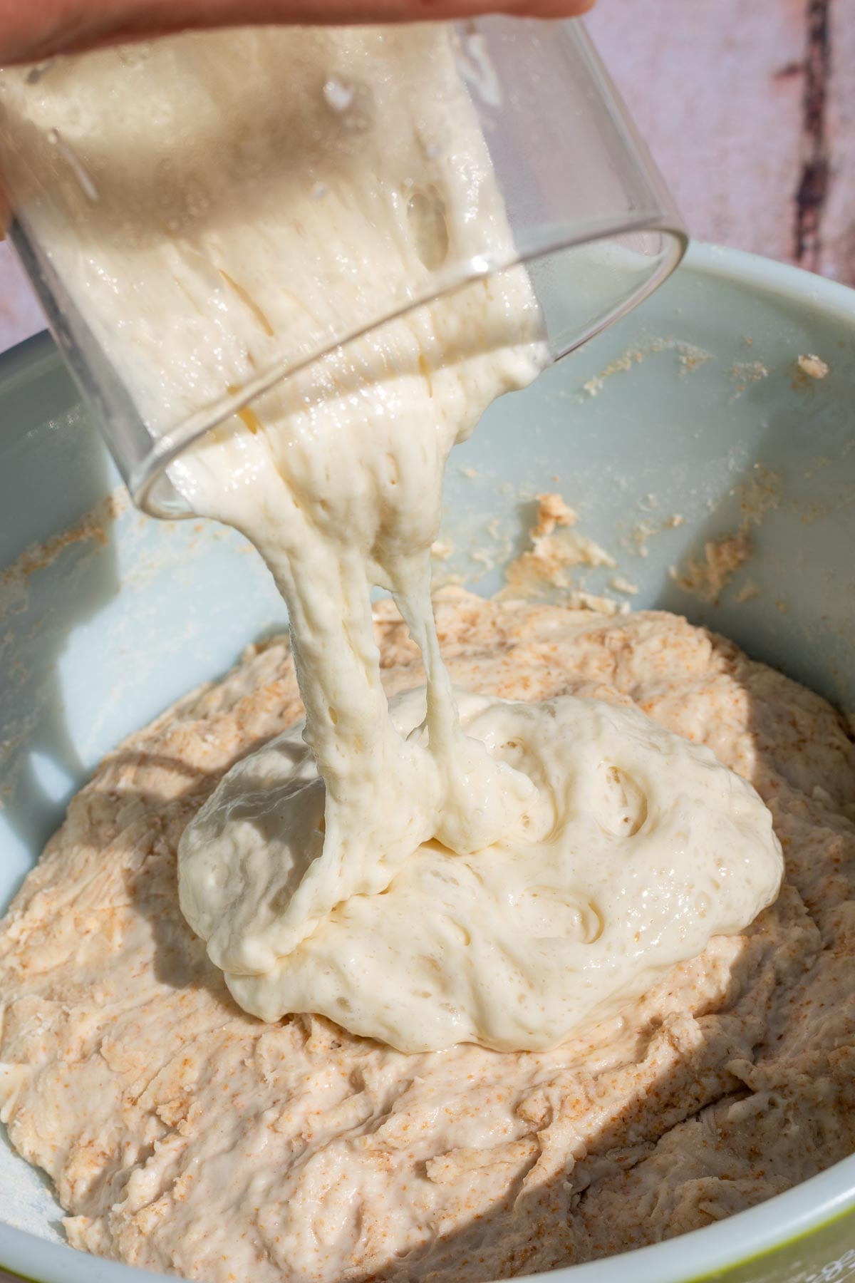 Pouring levain or sourdough starter into a mixing bowl with flours.