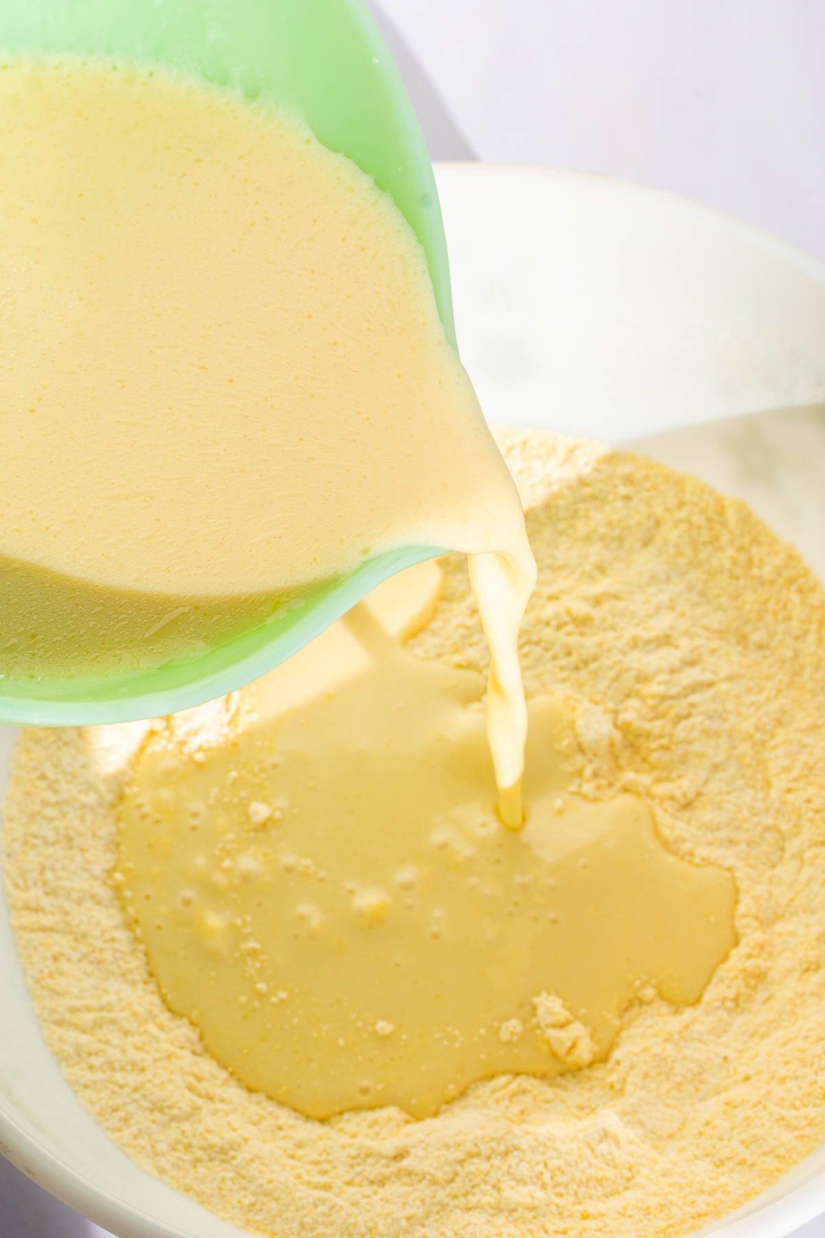 Pouring bowl of wet ingredients into bowl of dry ingredients.