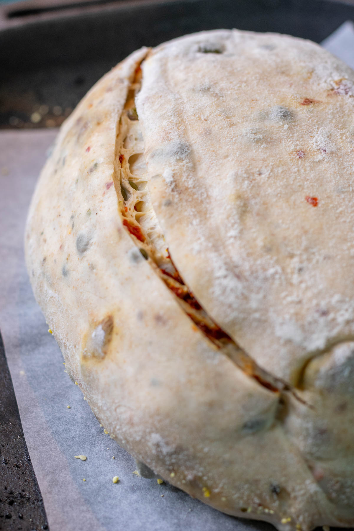 Scored sun-dried tomato sourdough bread on baking pan.