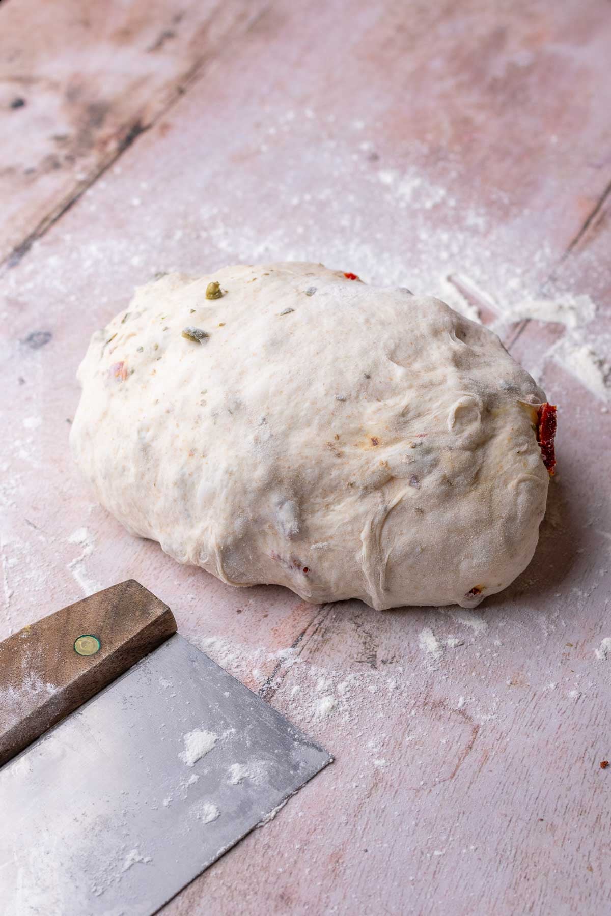 Shaped sun-dried tomato sourdough bread on counter with bench scraper.