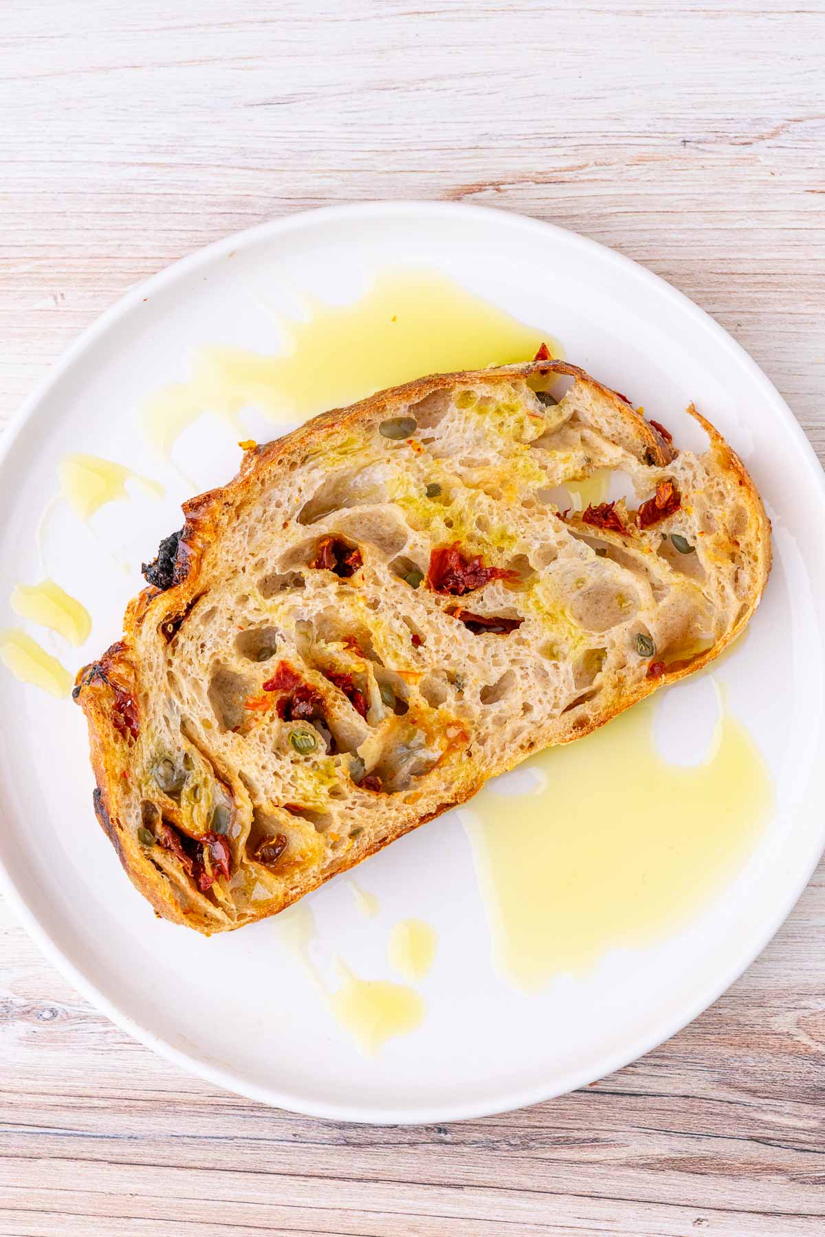 Slice of sun-dried tomato sourdough bread on a plate with olive oil.