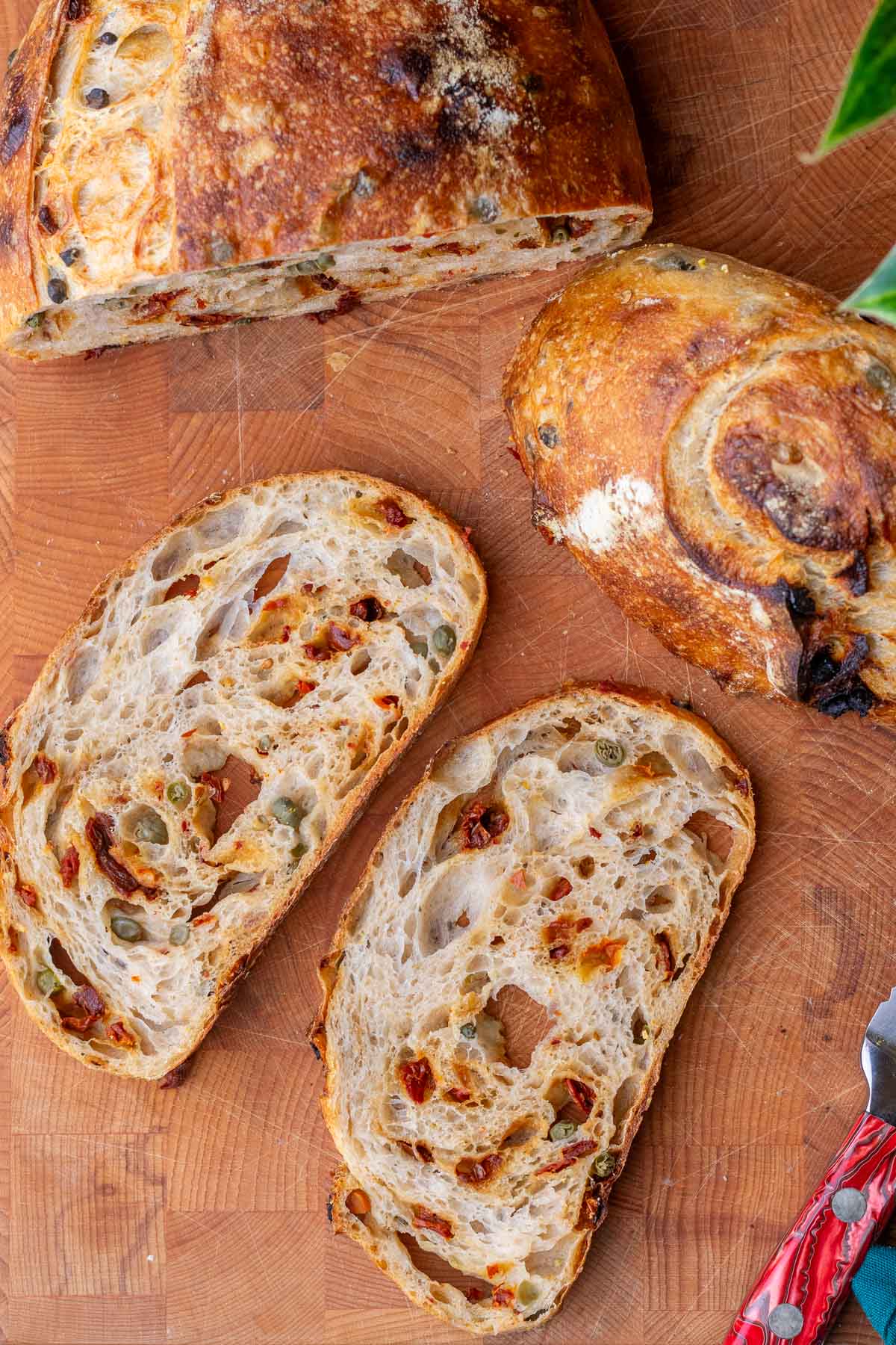 Slices of sun-dried tomato sourdough bread with capers on a cutting board.