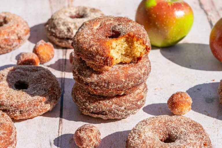 A stack of Sourdough Apple Cider Donuts coated in cinnamon sugar with a bite taken out of one.