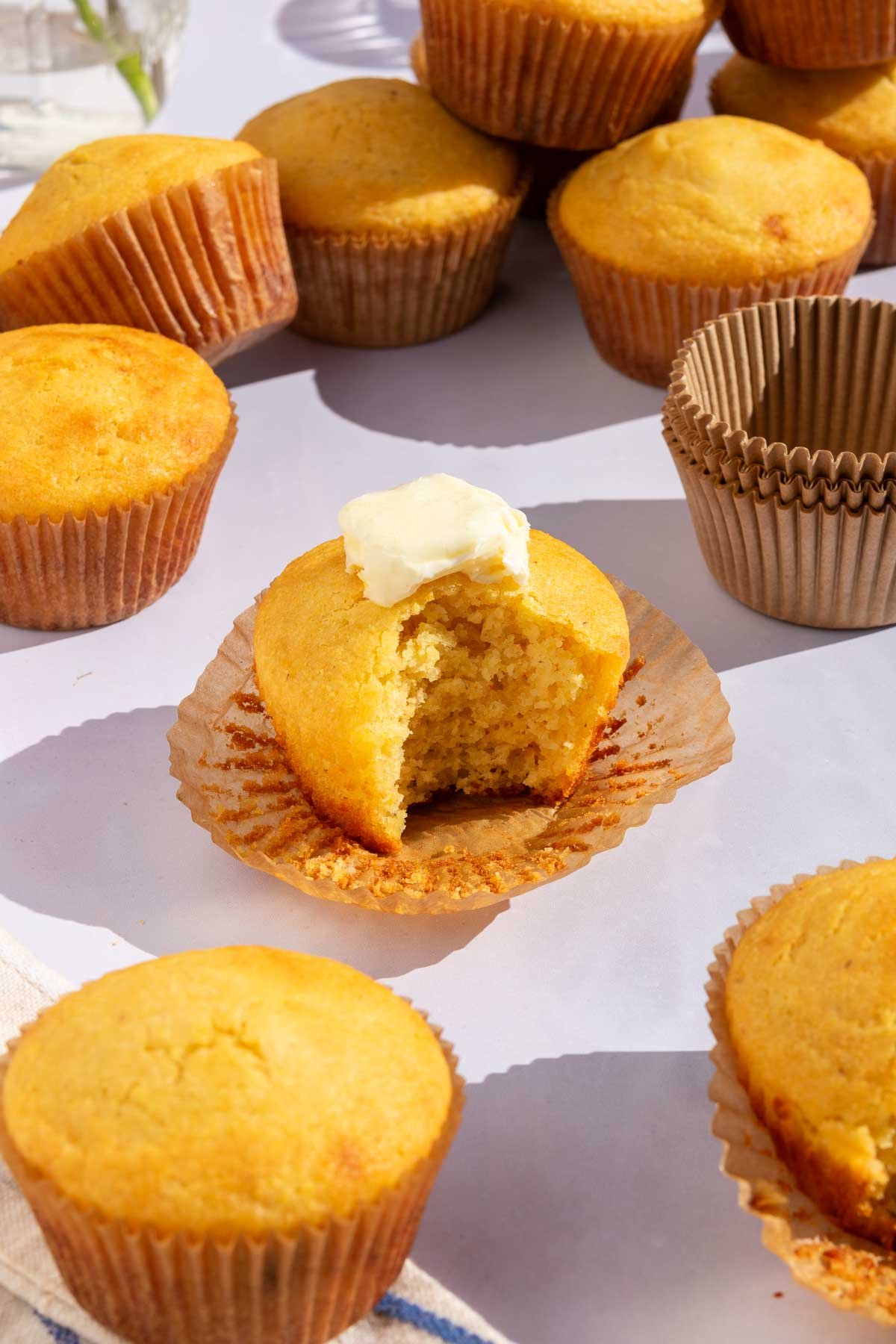 Sourdough corn muffins with one in the middle with a bite taken out of it and melting butter on top.