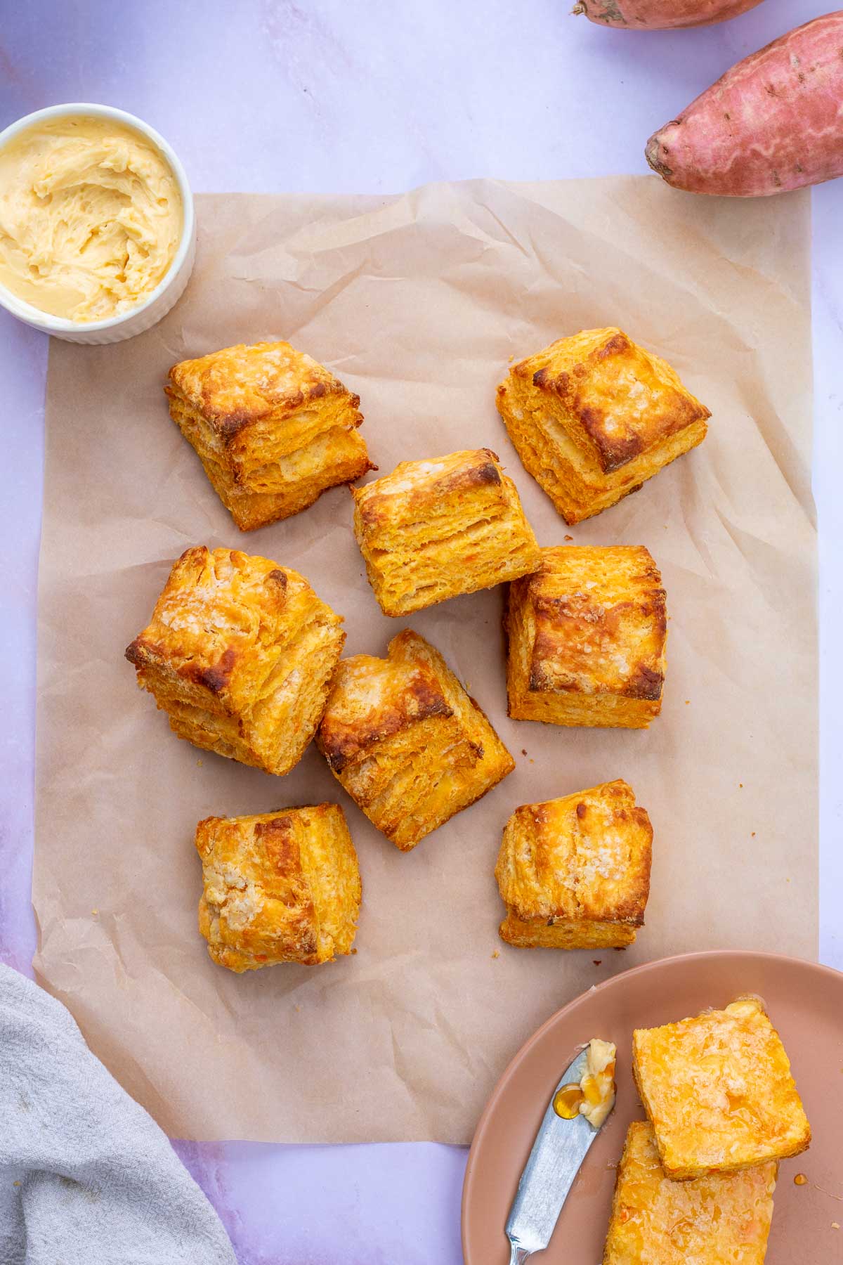 Sourdough sweet potato biscuits on parchment paper with a bowl of hot honey butter.