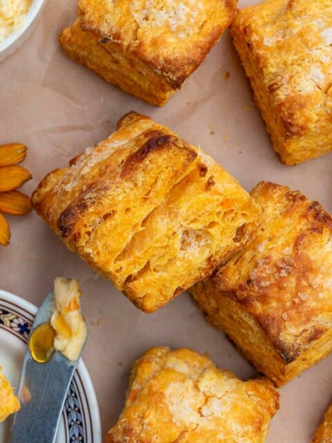 Flaky sourdough sweet potato biscuits on parchment paper with hot honey butter.