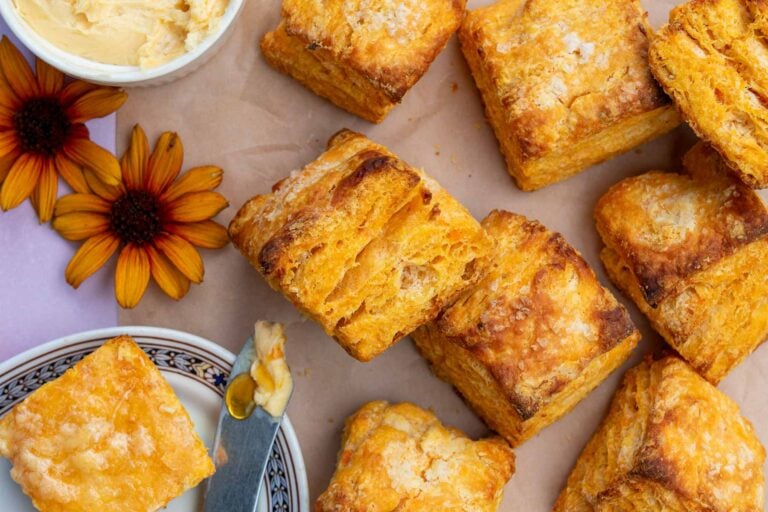 Flaky sourdough sweet potato biscuits on parchment paper with hot honey butter.