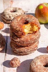 A stack of sourdough apple cider donuts with a cinnamon sugar coating and a bite taken out of the top one.