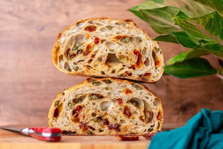 Sun-dried tomato sourdough bread with capers, red pepper flakes, and oregano sliced in half and stacked on top of each other.