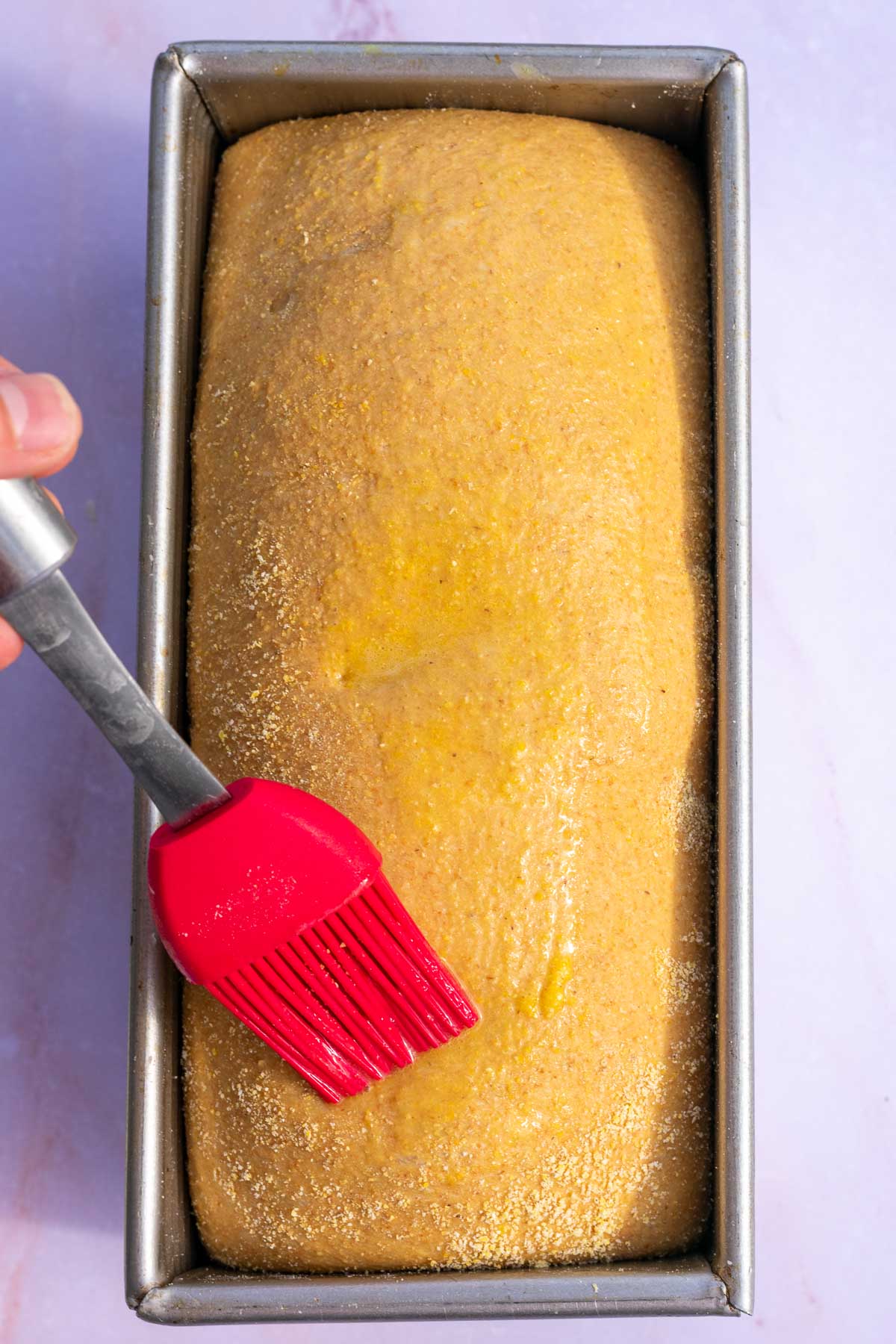 Brushing egg wash on top of sourdough anadama bread.