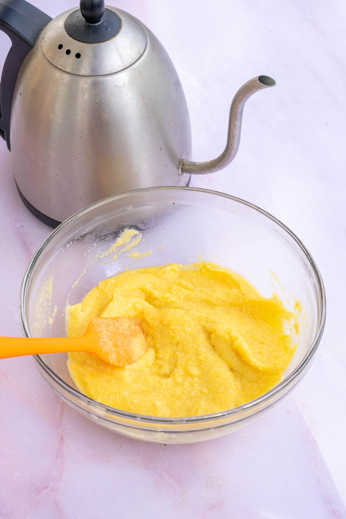Bowl of cornmeal porridge mixed with a spatula and a tea kettle in the background.