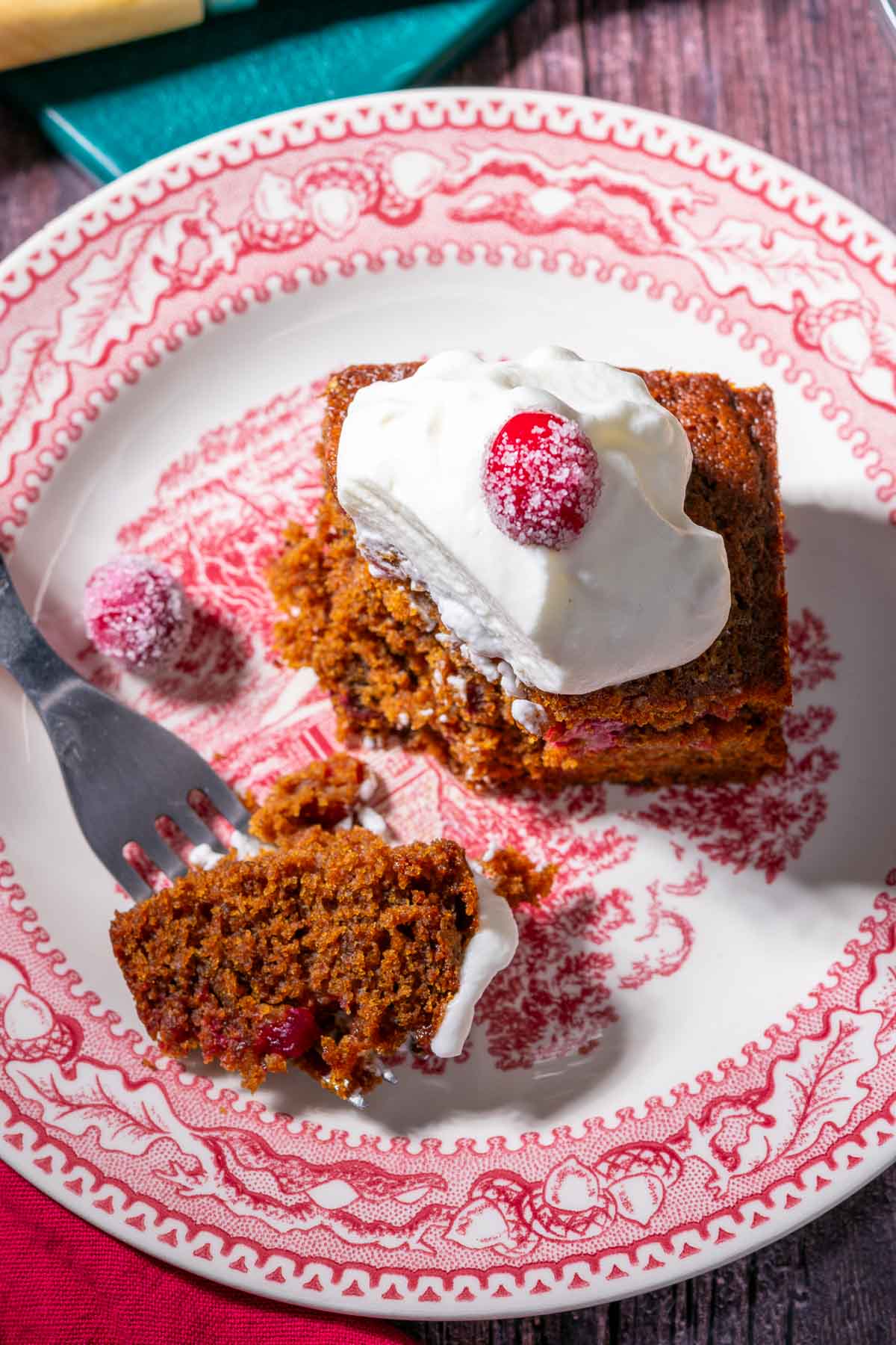 Sourdough gingerbread cake with whipped cream and cranberries on a plate with a fork with a bite taken out of it.
