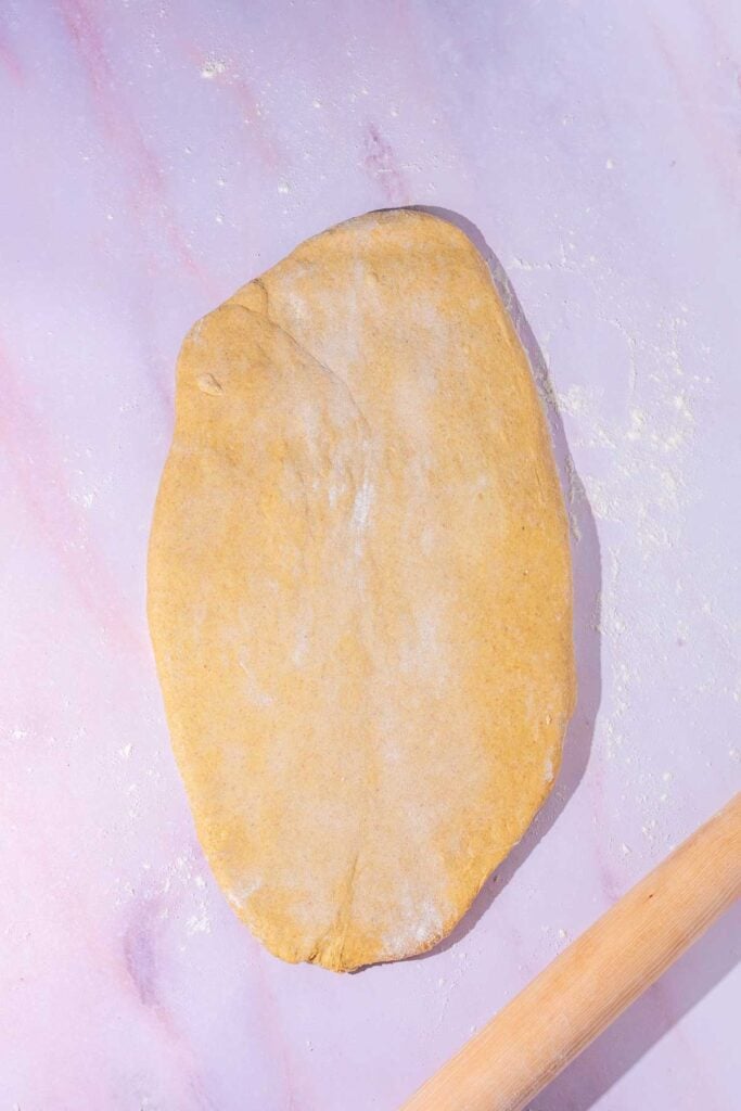 Sourdough anadama bread rolled out into a flat oval with a rolling pin.