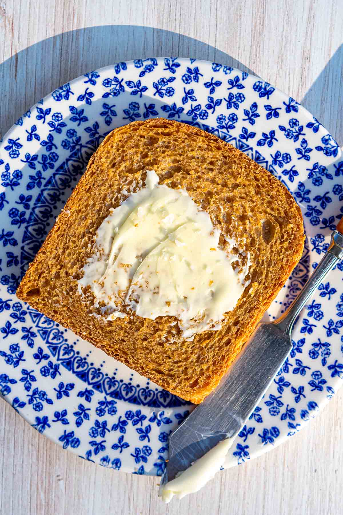 A slice of sourdough anadama bread on a plate with butter and flaky salt.