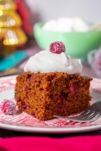 Slice of sourdough gingerbread cake with cranberries and whipped cream on a plate.