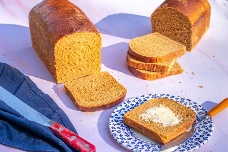 Two loaves of sliced sourdough anadama bread with one slice on a plate with butter.