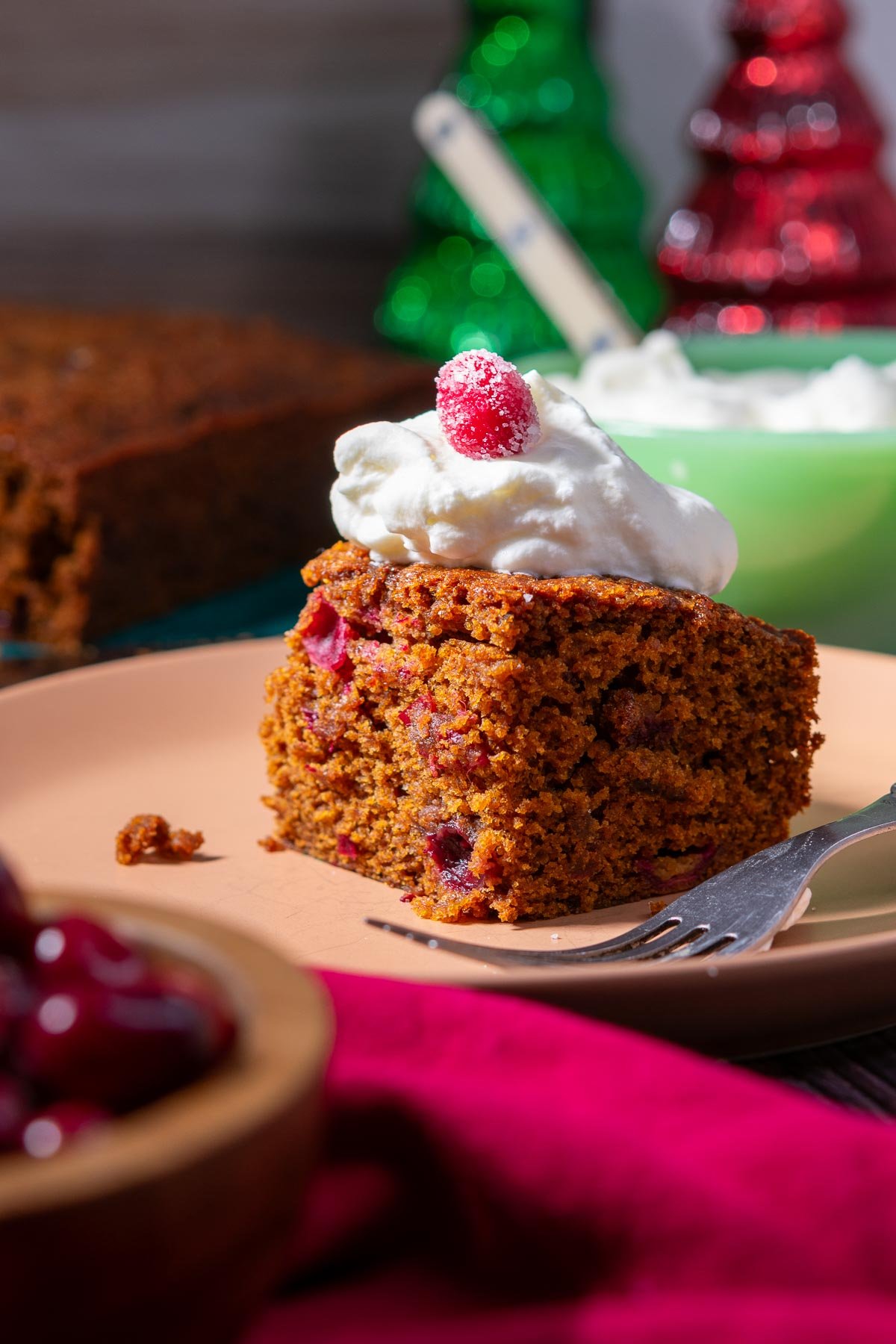 Slice of sourdough gingerbread cake with whipped cream and sugared cranberries on a plate.