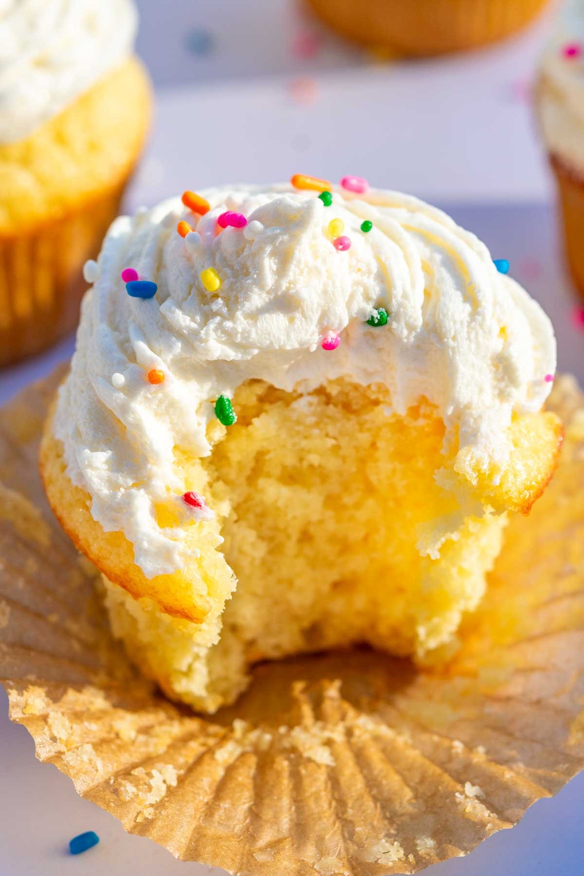 Close up of a sourdough cupcake with a bite taken out of it with rainbow sprinkles.