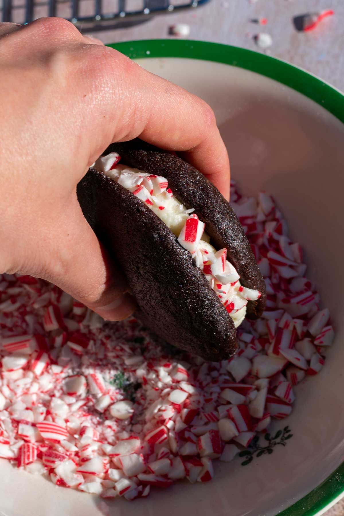 Hand coating a sourdough chocolate whoopie pie in a bowl of crushed candy canes or peppermint.