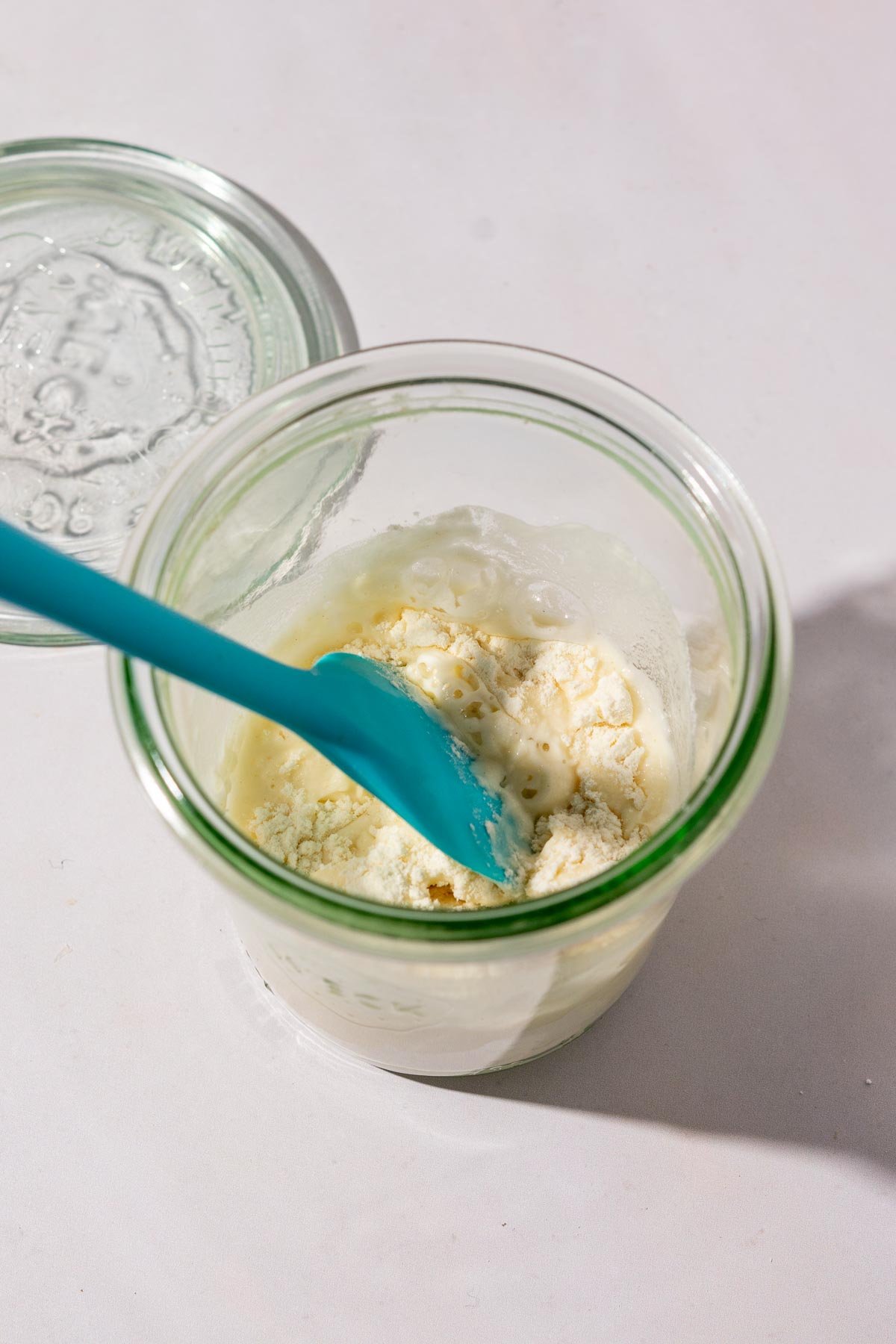 Feeding a small sourdough starter in a jar with a spatula.