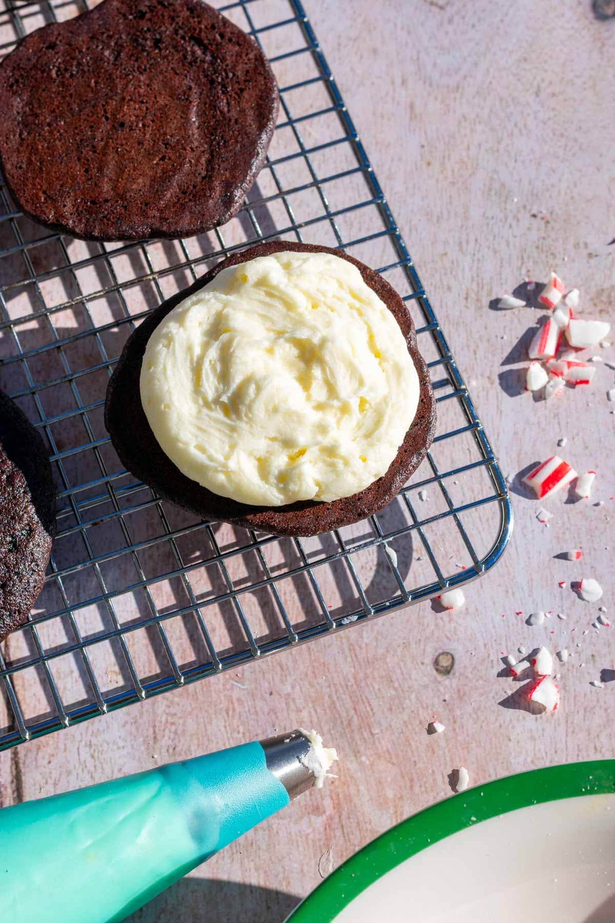 Piping peppermint buttercream filling in sourdough whoopie pie with crushed candy canes.