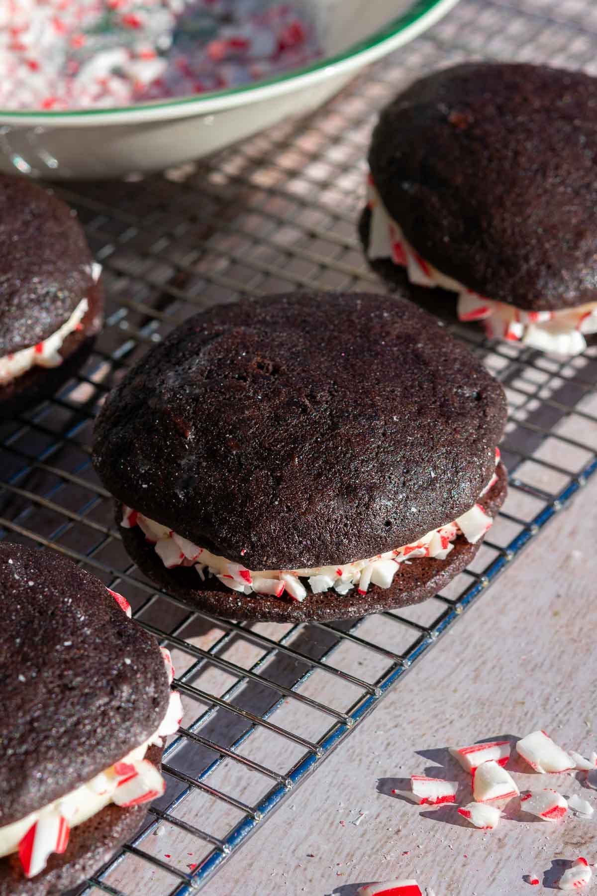 Sourdough chocolate peppermint whoopie pies on a wire rack coated with crushed peppermint.