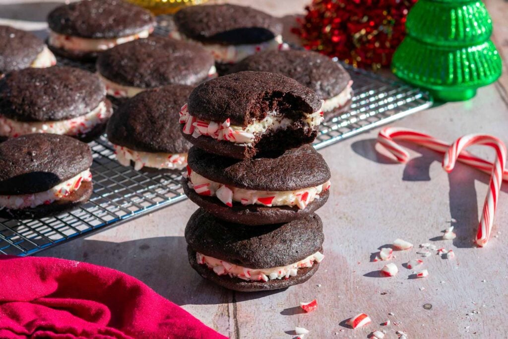 Sourdough chocolate peppermint whoopie pies stacked on top of each other with a wire rack and candy canes in the background.